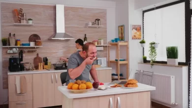 Modern kitchen trends that are the rage in 2025 featuring textured wood backsplash, light wood cabinets, and a functional island where a couple enjoys breakfast.