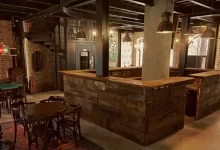 Rustic basement bar ideas with wood countertop, stone backdrop, and vintage lighting fixtures.