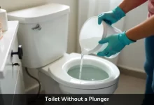 Person wearing rubber gloves using hot water to unclog a toilet without a plunger with dish soap and baking soda nearby