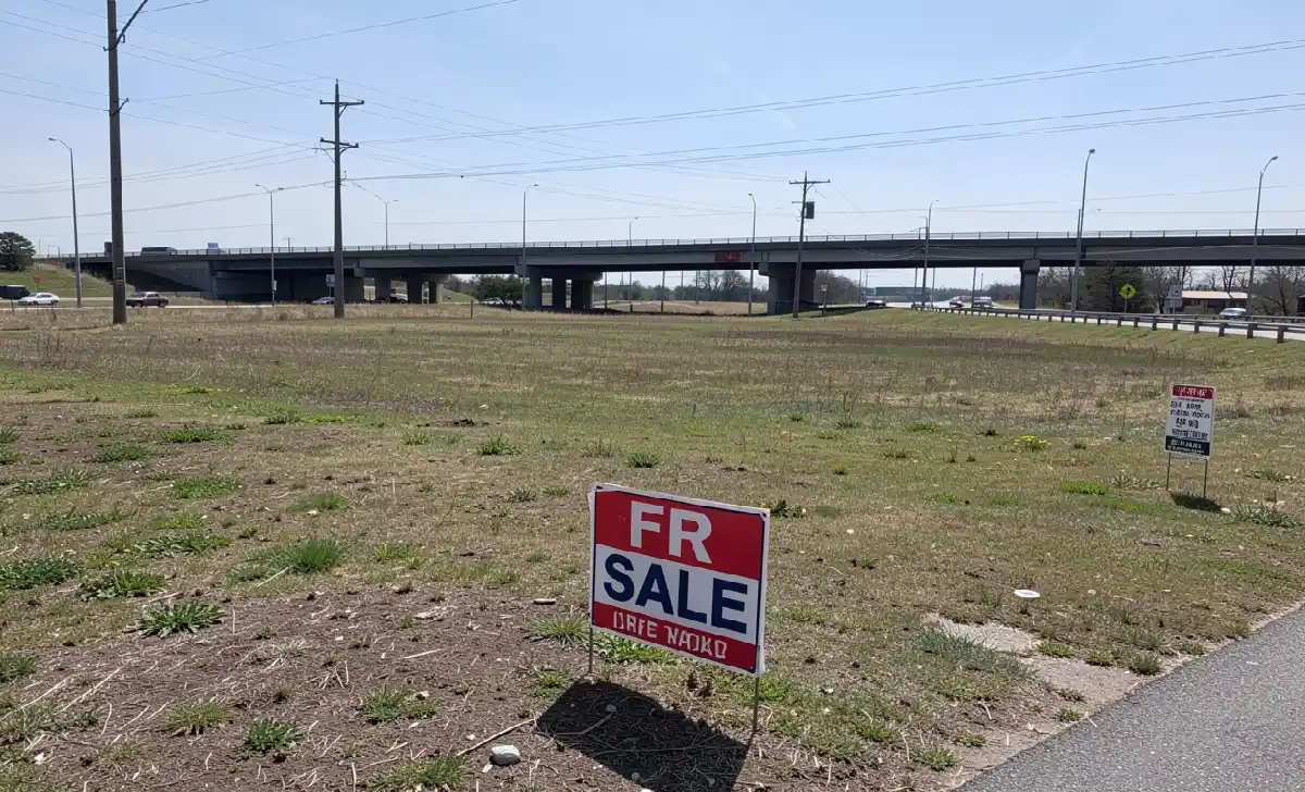 Commercial land for sale sign along a highway with open acreage in the background