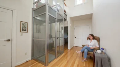 Modern Home Elevators with glass panels installed in a residential hallway next to a wooden staircase