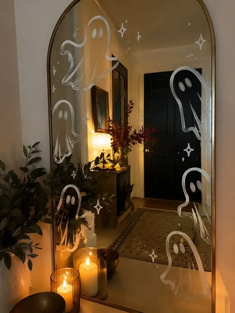 White chalk-marker ghost drawings on a large entryway mirror surrounded by warm, understated Halloween decor.