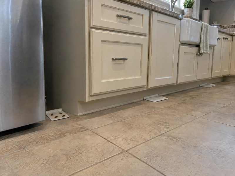 Cockroach monitoring traps in a residential kitchen, with several cockroaches caught beside the refrigerator and empty traps beneath the cabinets